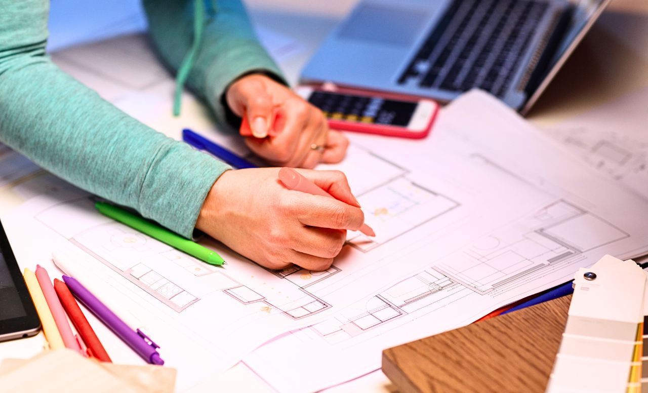 Personne en train de dessiner ou annoter des plans d’aménagement intérieur avec stylos colorés.